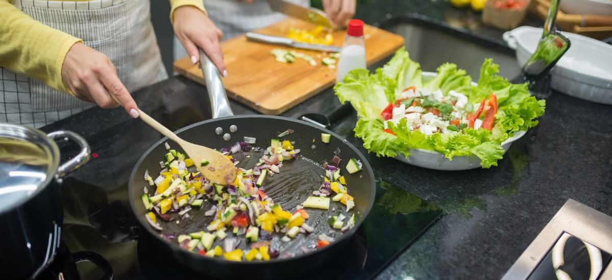 Two adults cooking fresh vegetables on a stove, preparing a healthy meal in a modern kitchen.