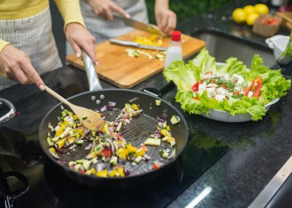 Two adults cooking fresh vegetables on a stove, preparing a healthy meal in a modern kitchen.