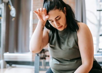 Overweight woman with dark hair in sportswear wiping sweat from face while training in gym in daytime