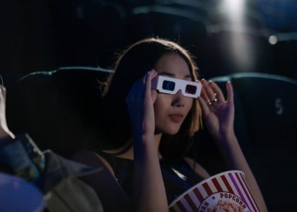 Asian woman wearing 3D glasses, enjoying popcorn in a movie theater.